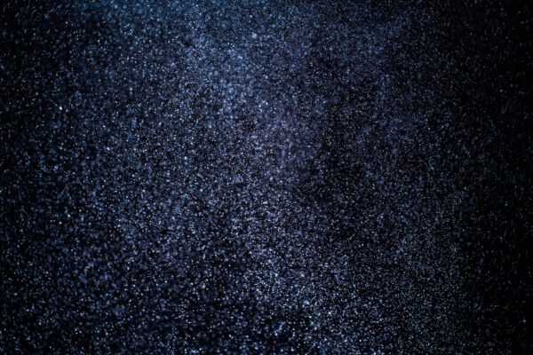 Organic dust particles floating on a colorful light beam on black background.